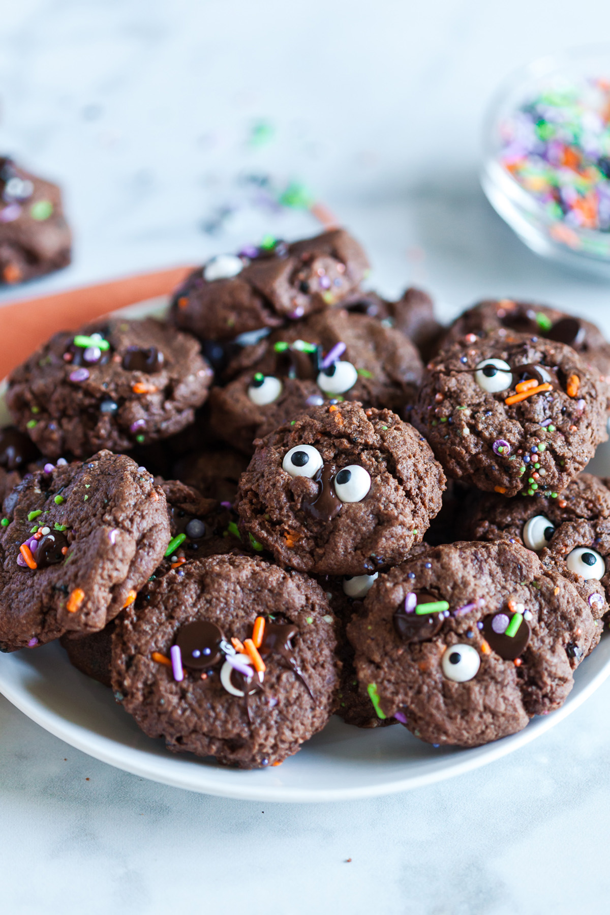Plate of chocolate cookies with candy eyes and Halloween sprinkles, set on an orange napkin.