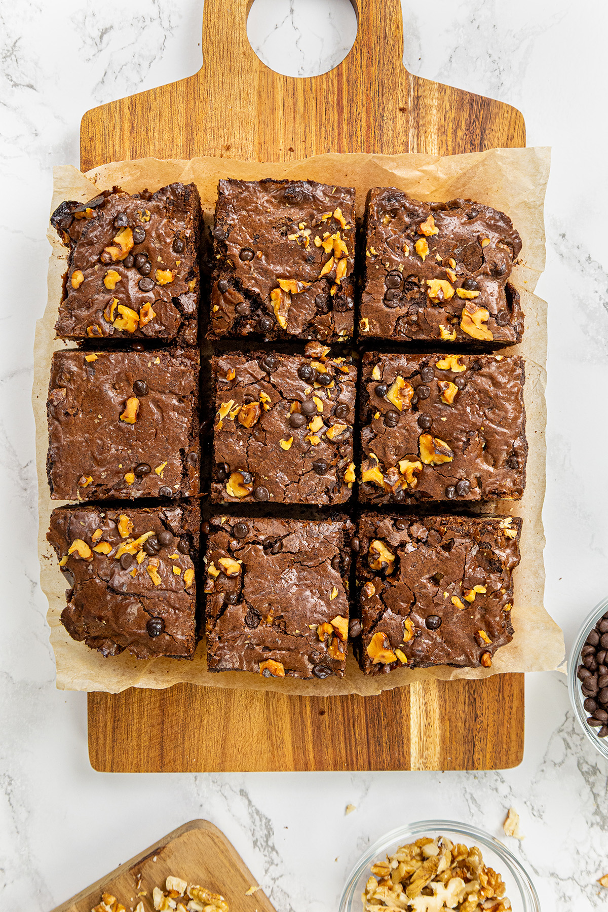 Freshly baked chocolate walnut brownies cut into nine squares on parchment paper on a wooden cutting board.