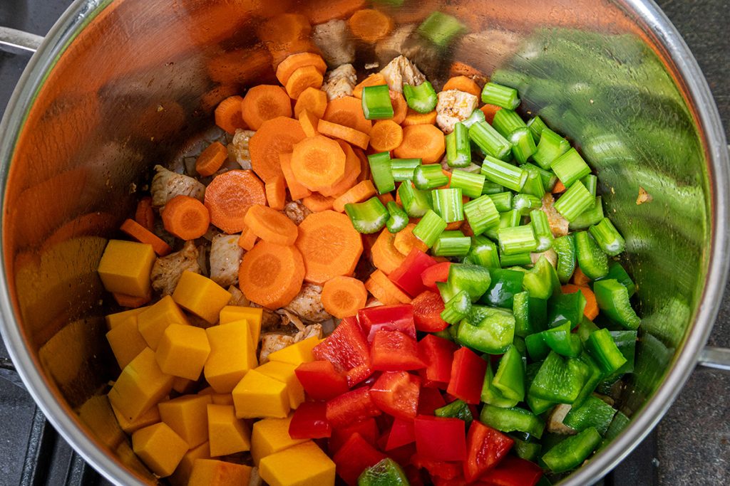 Carrots, celery, red pepper, green pepper, and butternut squash added to browned chicken in a pot for chicken vegetable soup.