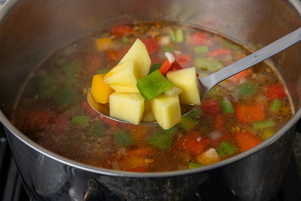 Large chunks of Yukon gold potatoes added to simmering chicken vegetable soup with vegetables and broth.