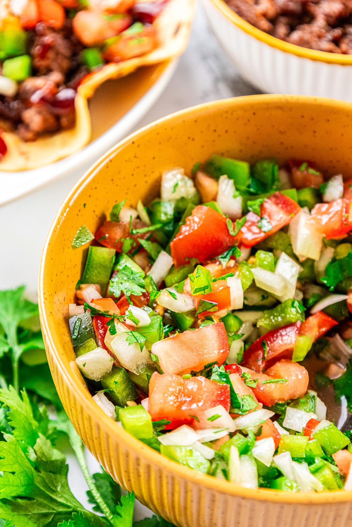 Close-up of a yellow bowl filled with colorful Pebre made with chopped tomatoes, green bell peppers, onions, and cilantro.