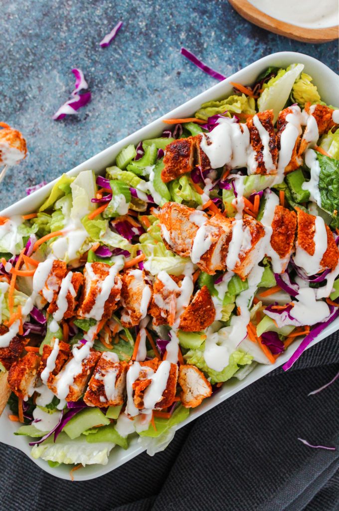 Lettuce and buffalo chicken tenders in a large serving dish.
