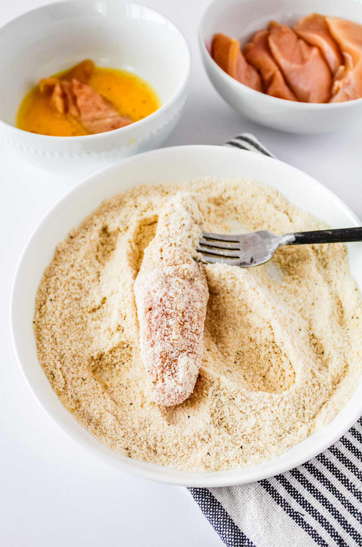Dipping a chicken tenderloin into breading.