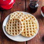 Dash mini waffles on a plate with Dash waffle maker in background.