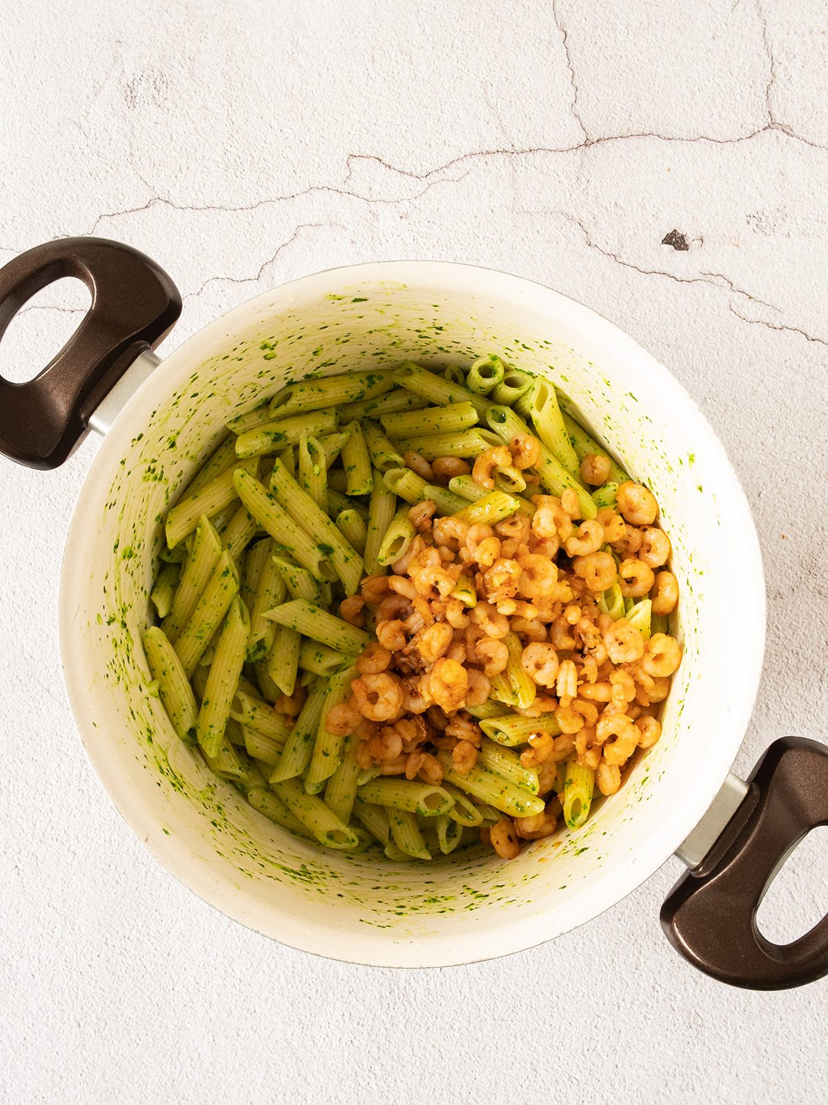 Shrimp added to pasta and sauce in a bowl.