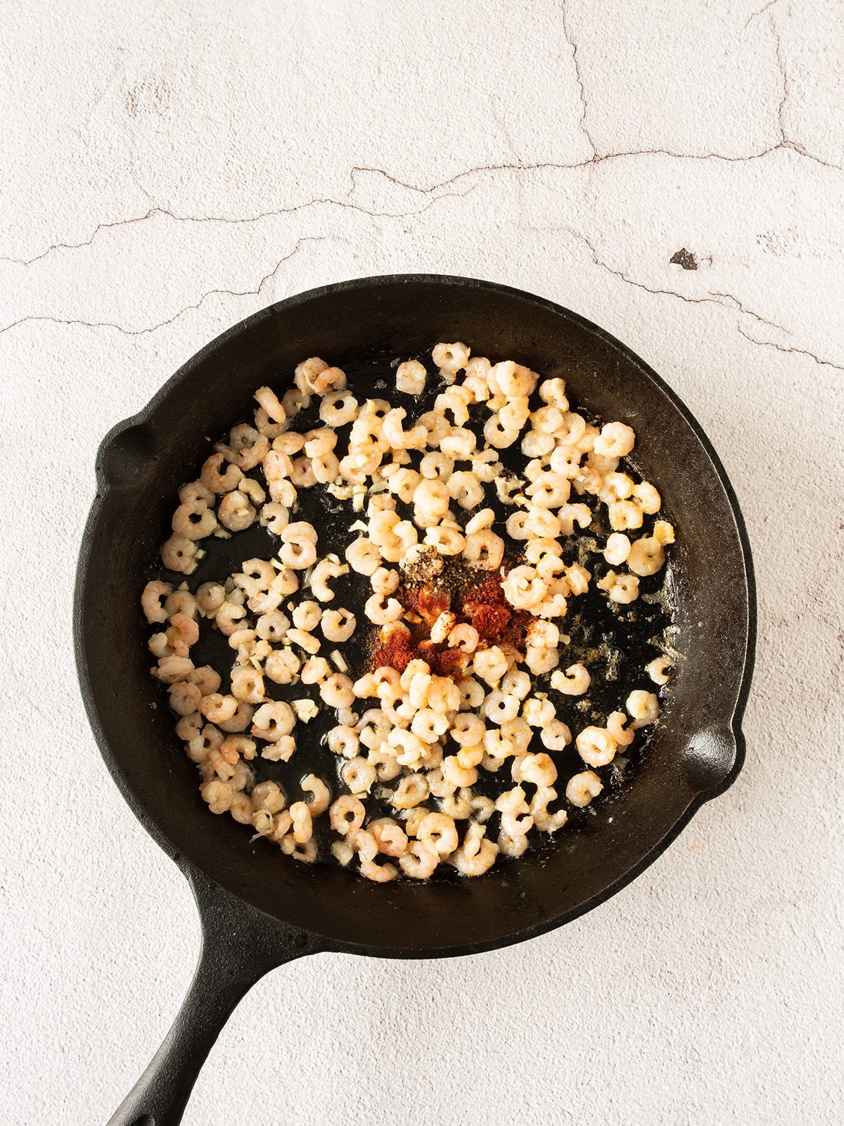 Raw shrimp with seasoning in a skillet.