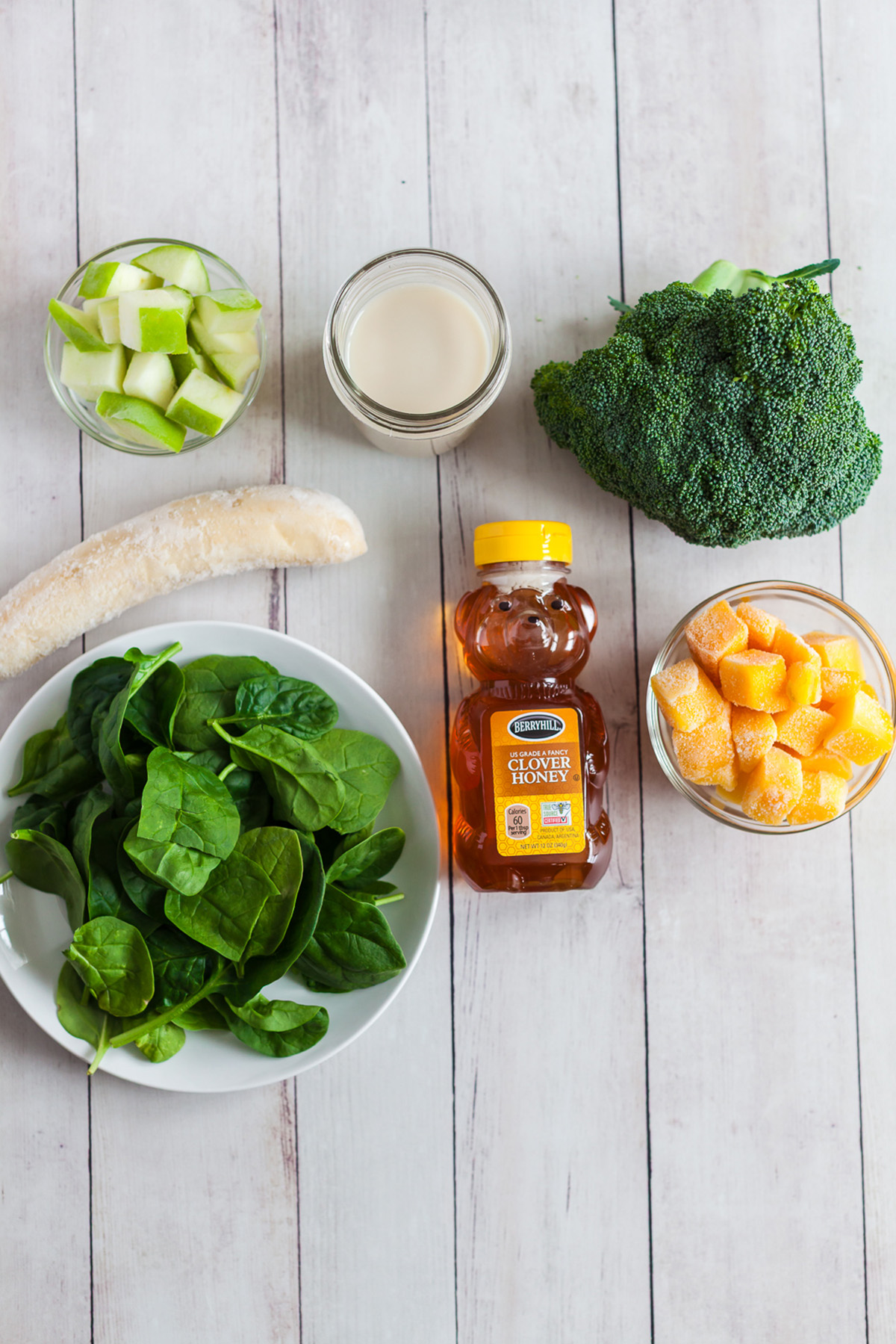 Broccoli, apple, mango, spinach, banana and almond milk with honey on the counter.