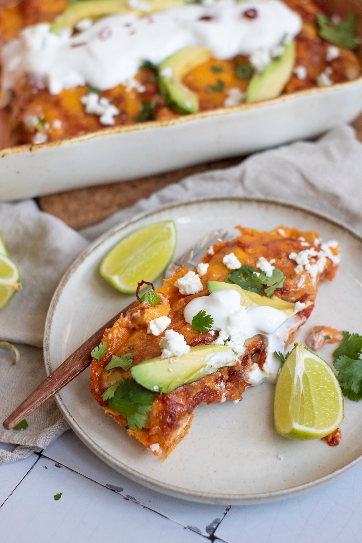 Black bean and rice enchiladas on a plate with lime wedge and garnishes.