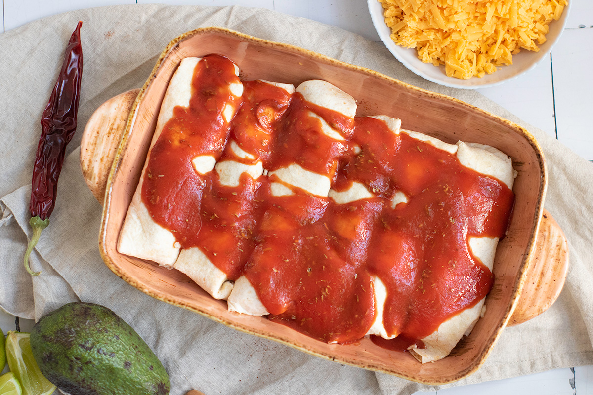 Add enchilada sauce on top of enchiladas in a pan.