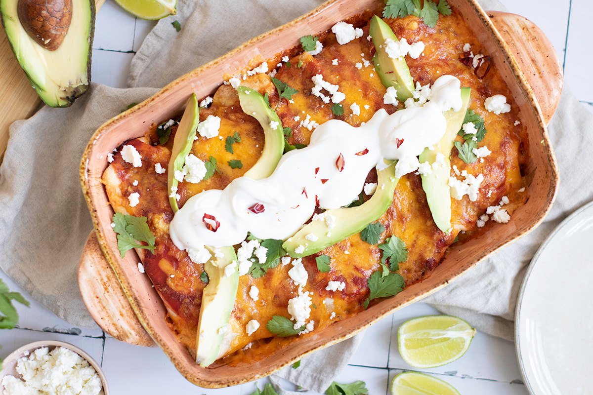Black bean and rice enchiladas topped with sour cream, avocado and cilantro.