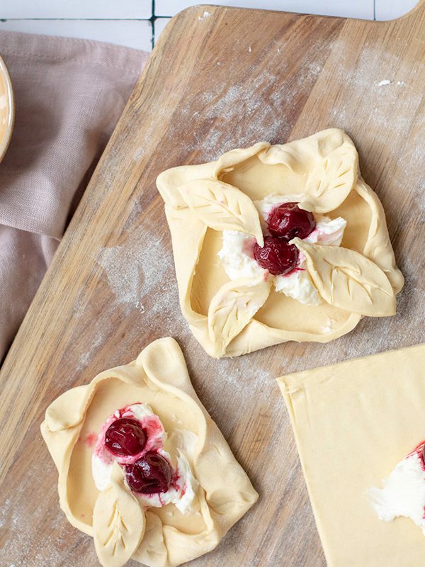 Showing how to put cream cheese and cherry on the puff pastry and wrap into danish.