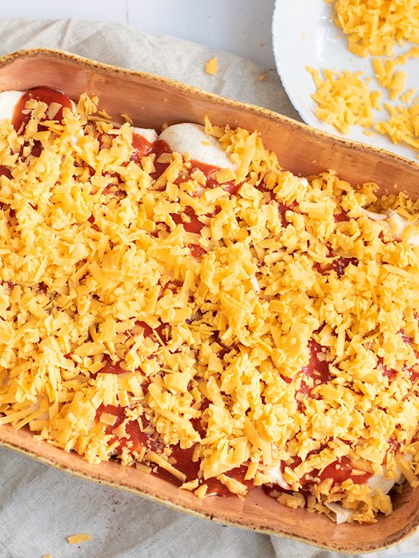Topping unbaked black bean and rice enchiladas with cheese.