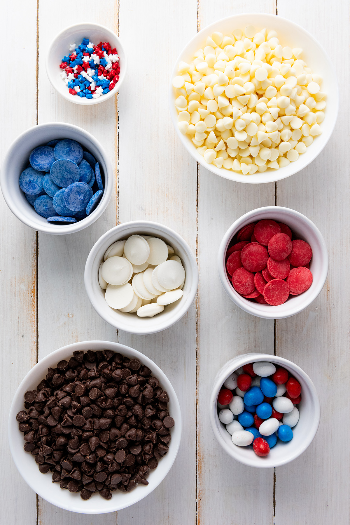 A flat lay of 4th of July bark ingredients including star sprinkles, white chocolate chips, blue candy melts, red candy melts , white candy melts, chocolatechips and red, white and blue M&Ms.