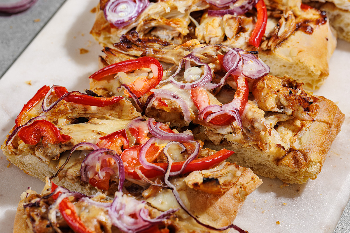 Close-up of sliced BBQ chicken flatbread topped with melted cheese, caramelized onions, and roasted red peppers.