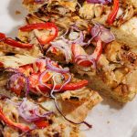 Slices of BBQ chicken flatbread arranged on a white board, showing crisp edges and gooey cheese.