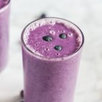 Close-up of a blueberry smoothie made with cauliflower in a clear glass with fresh blueberries on top.