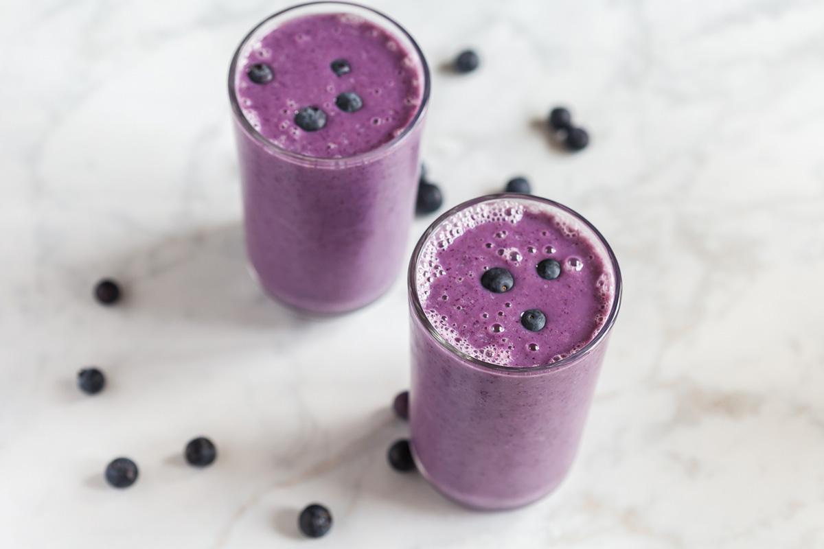 Two tall glasses of blueberry cauliflower smoothie with scattered blueberries on a marble counter.