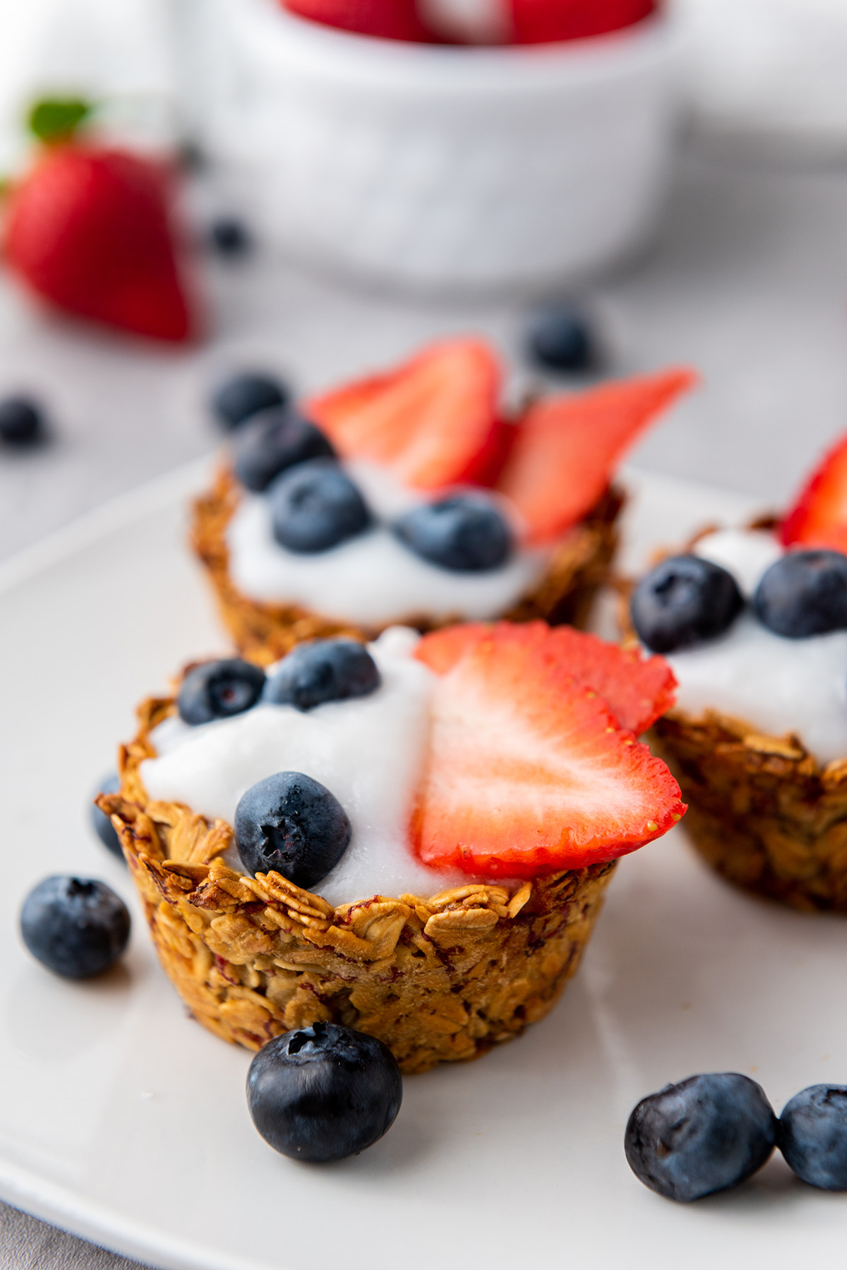 Side angle of a yogurt granola cup topped with fresh berries, highlighting the texture of the oat shell.