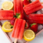 Frozen strawberry lemonade popsicles arranged on ice with fresh strawberries and lemon slices for garnish.