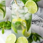 Close-up of a refreshing fauxjito mocktail in a tall glass with ice, lime slices, mint leaves, and a paper straw.