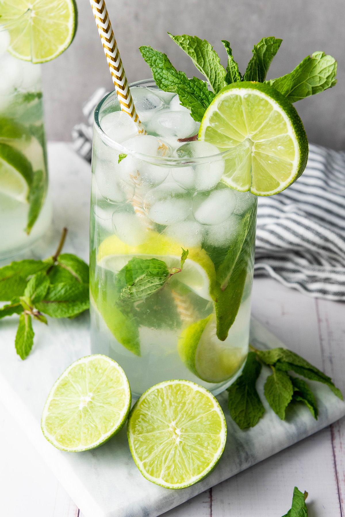 Close-up of a refreshing fauxjito mocktail in a tall glass with ice, lime slices, mint leaves, and a paper straw.