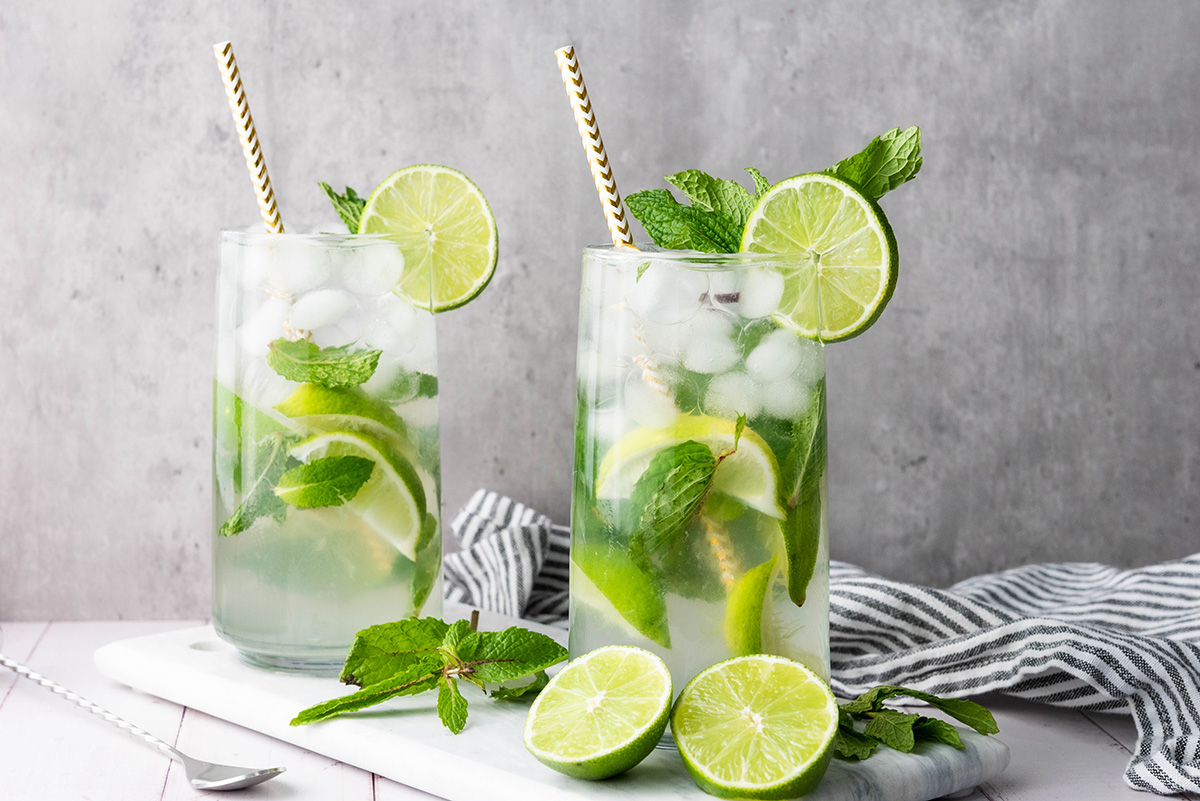 Two glasses of fauxjito mocktails garnished with lime wheels and mint, served with straws on a marble board.