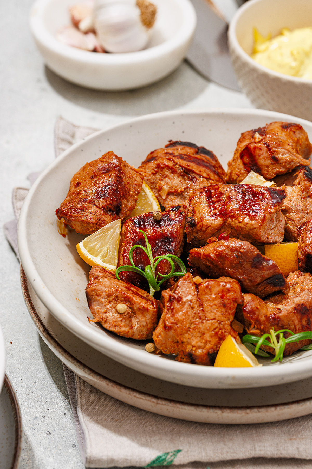 Close-up of juicy grilled pork tenderloin pieces in a bowl with lemon wedges and fresh herbs, ready to serve.