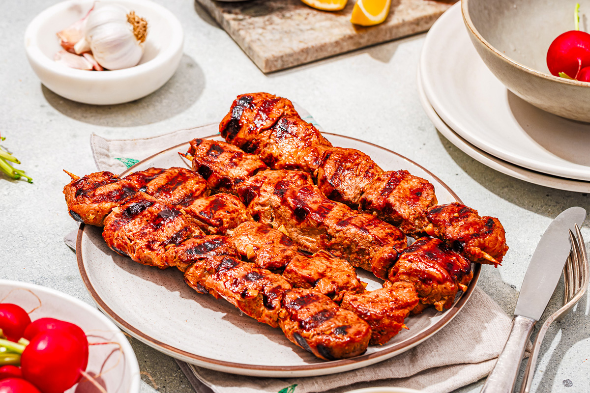 Pork tenderloin skewers grilled to perfection, served on a plate next to radishes and garlic.