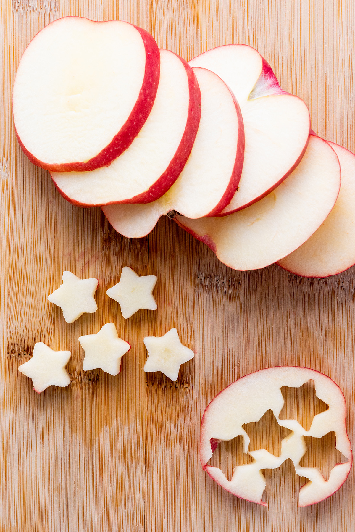 Apple slices on a wooden board with star-shaped apple cutouts, ready for a festive star-spangled fruit salad.