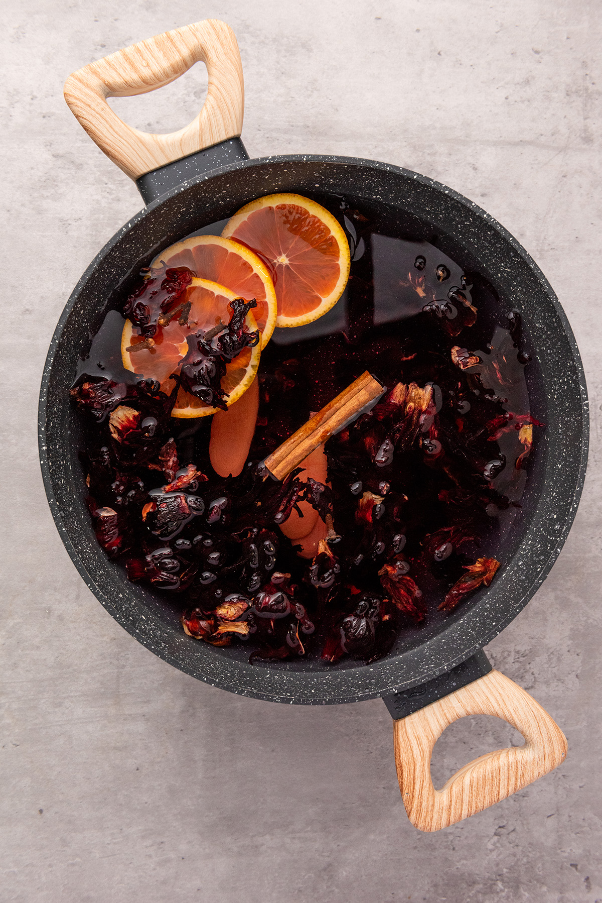 A pot of water simmering with dried hibiscus petals, orange slices, and a cinnamon stick to make Mexican hibiscus tea.