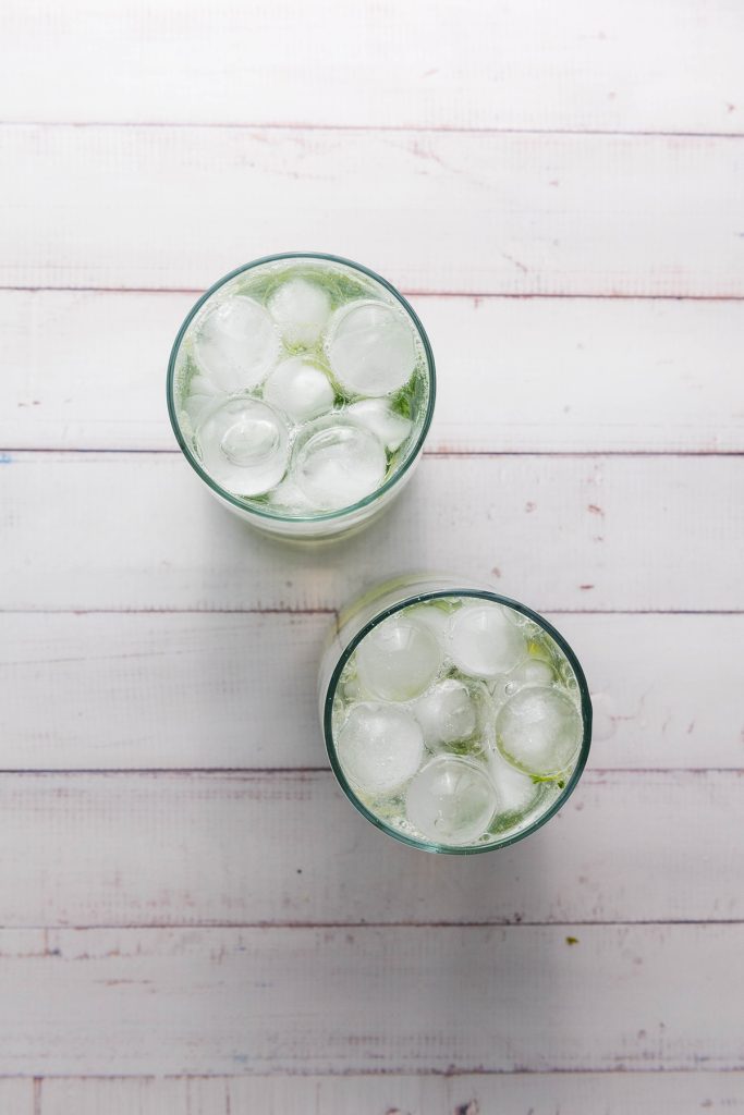 Two glasses filled with ice over muddled mint and lime, with club soda to complete the fauxjito.