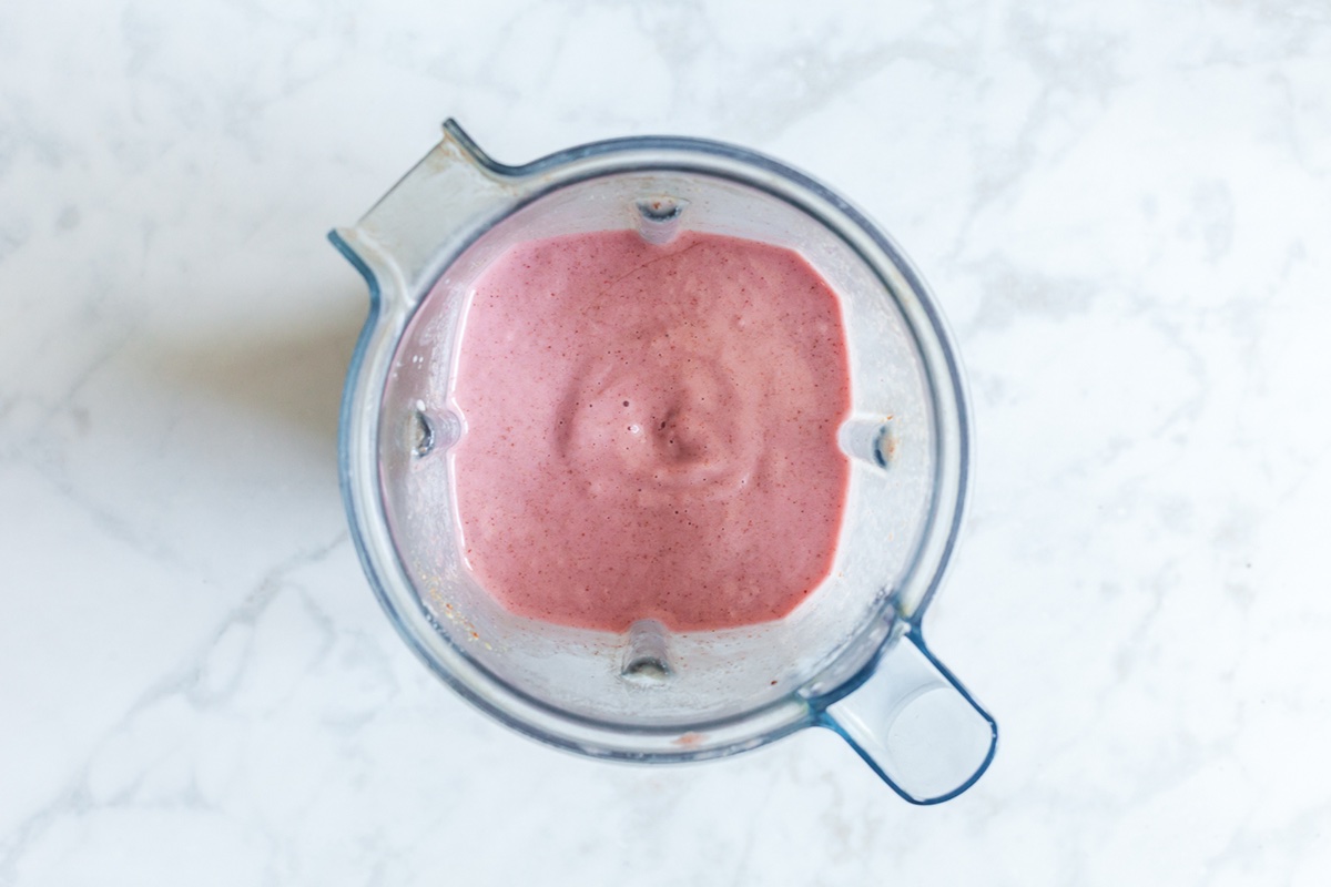 Strawberry banana flaxseed smoothie fully blended and creamy inside a blender on a marble surface.