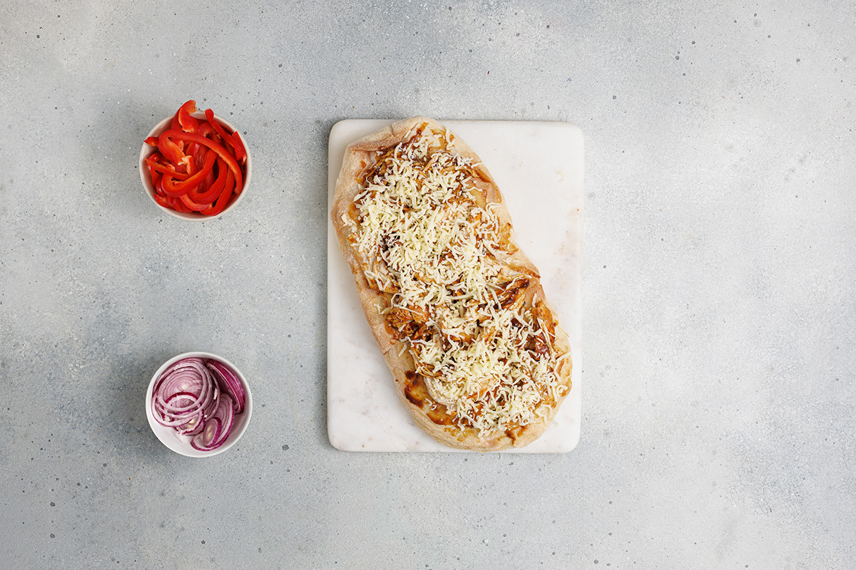Flatbread topped with BBQ chicken and shredded cheese, ready for more toppings.