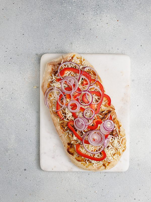 Flatbread with BBQ chicken, cheese, and freshly added sliced red onions and red peppers before baking.