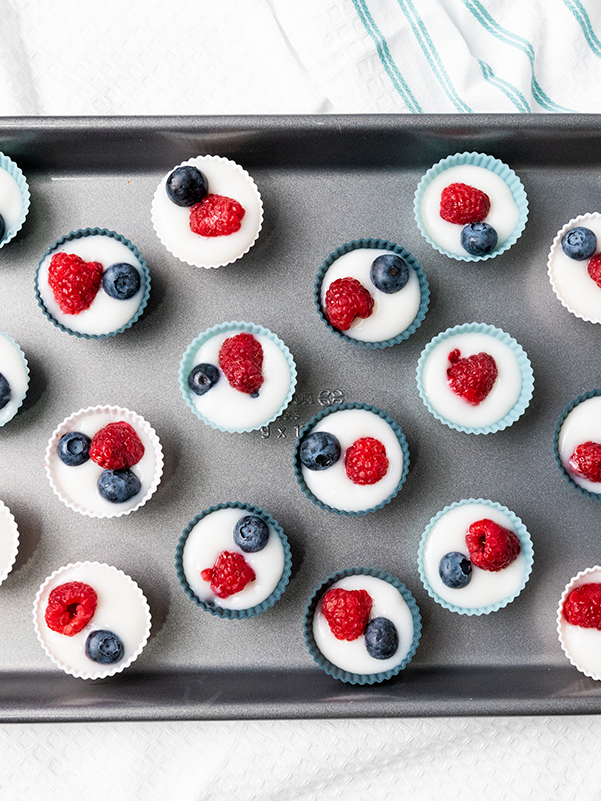 A baking tray filled with mini silicone cups of yogurt and berries, ready to be frozen into yogurt bites.