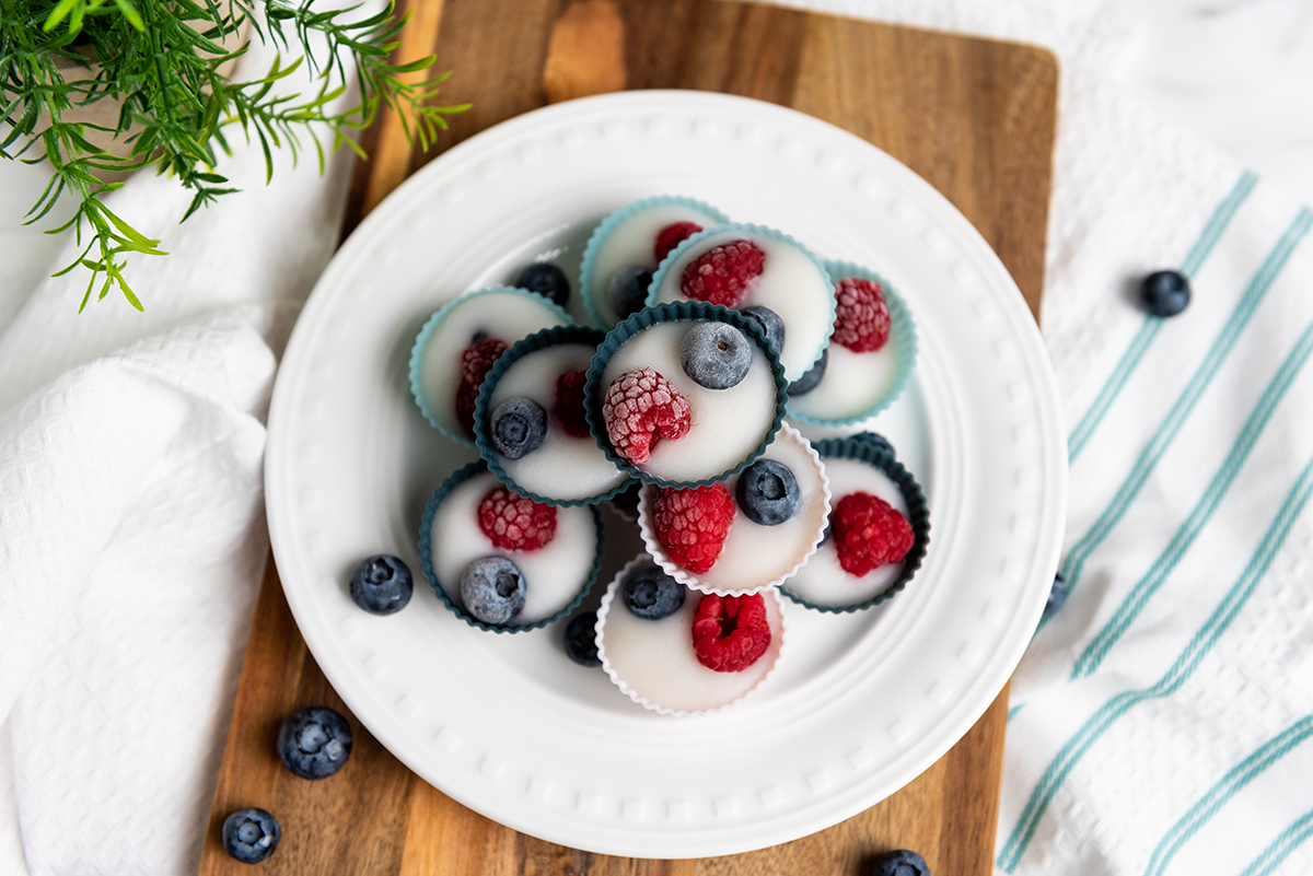 A plate stacked with frozen yogurt berry bites in colorful silicone liners, topped with raspberries and blueberries.