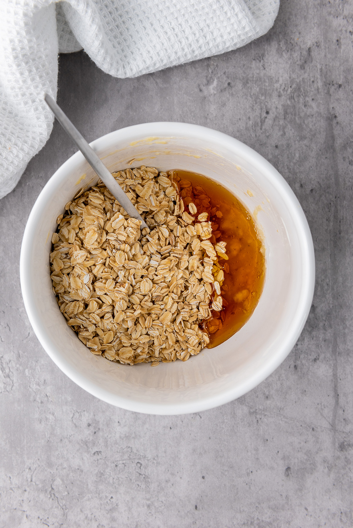 Rolled oats and honey added to the mashed banana in a bowl, ready to be stirred together for the granola base.