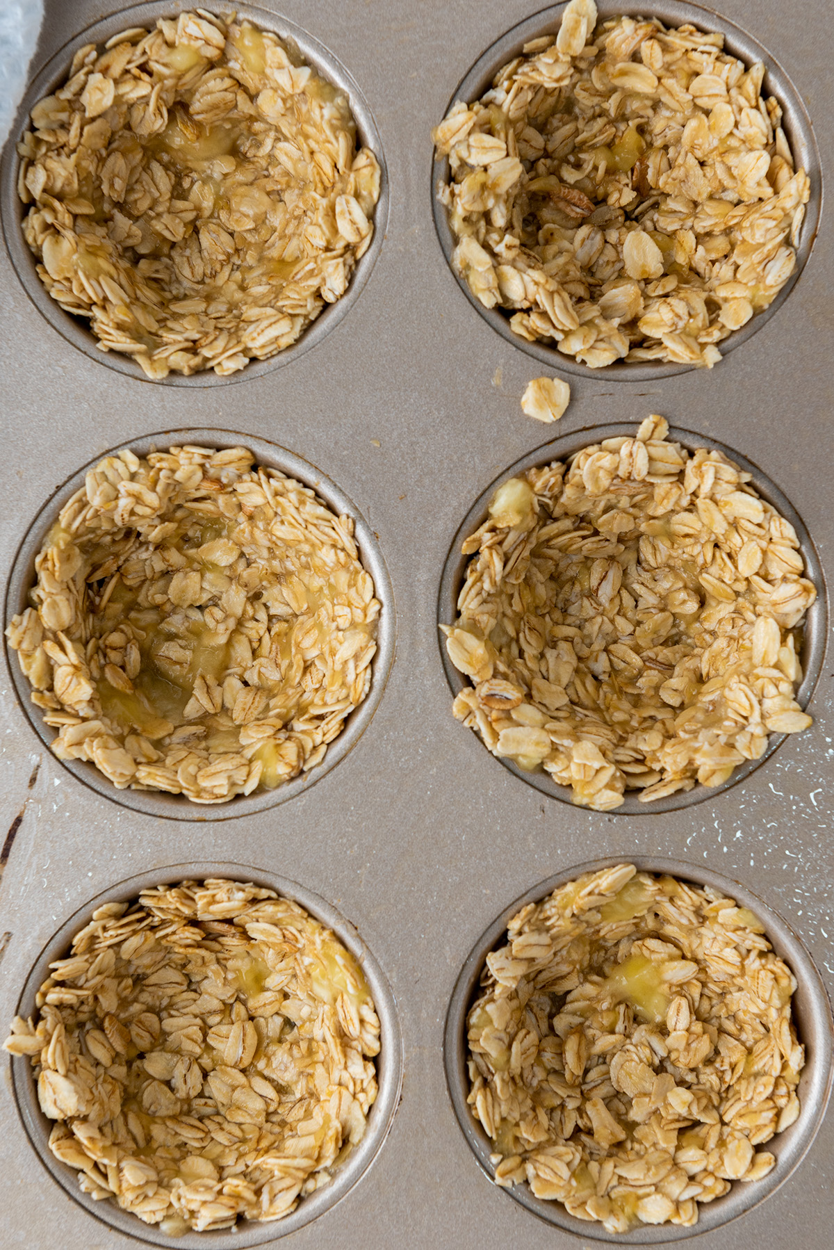 Granola mixture pressed into muffin tin cavities to form edible cups, ready to be frozen and baked.