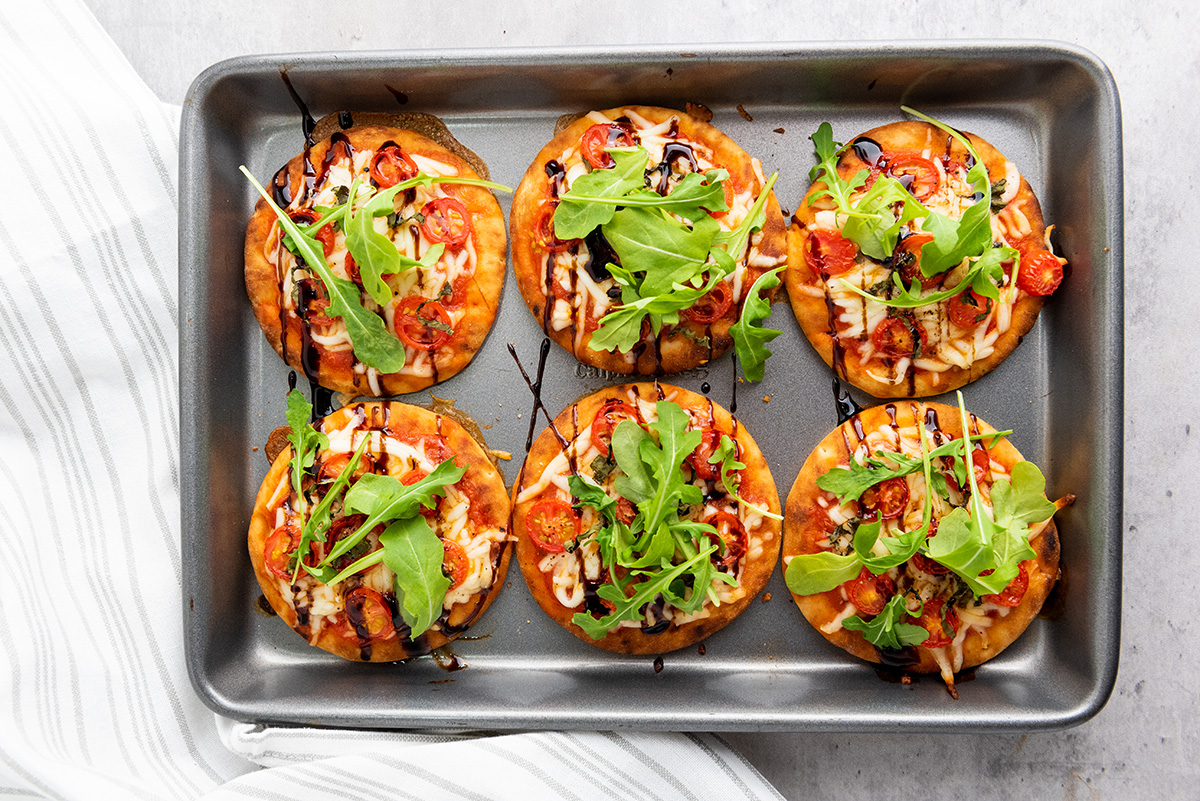 Finished mini Caprese pizzas topped with arugula and served on a baking tray, ready to eat.