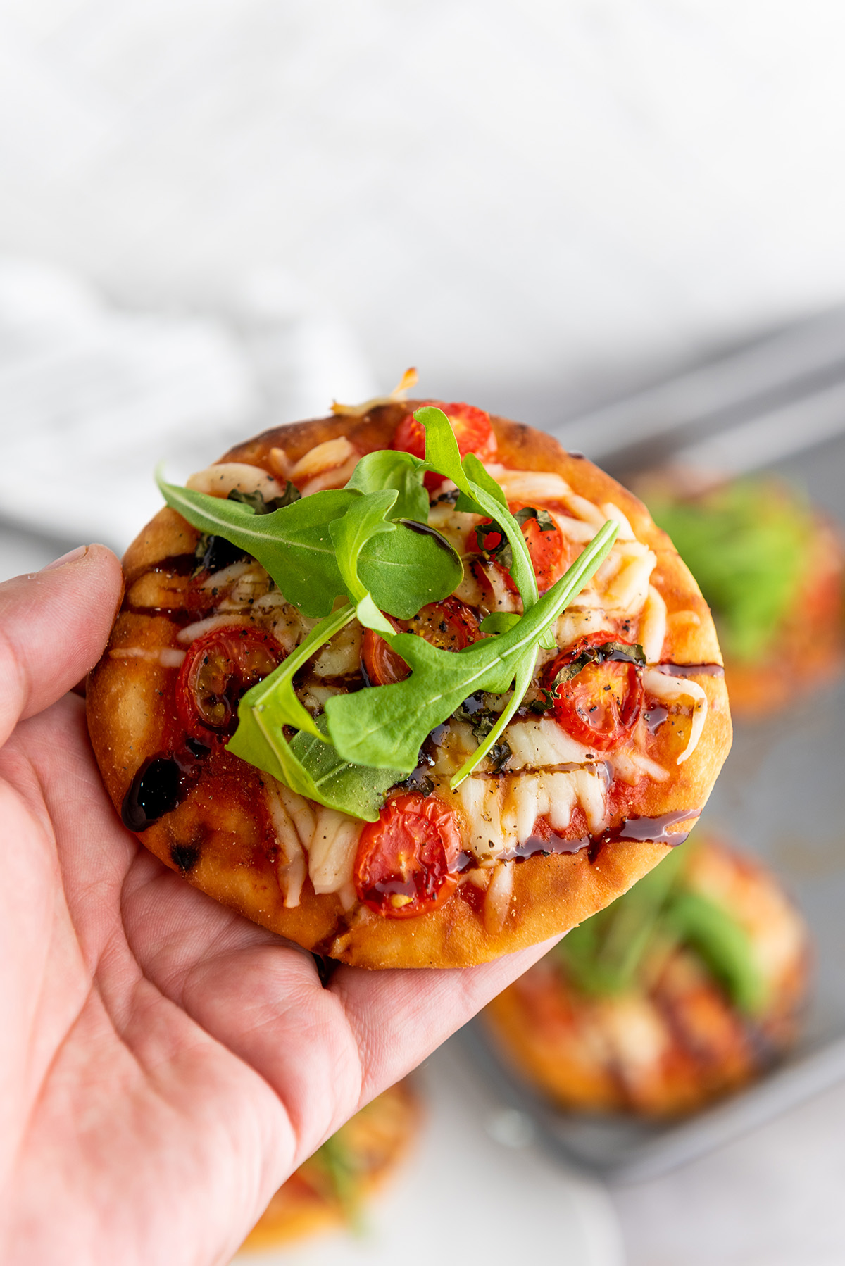 A hand holding a mini caprese pizza.