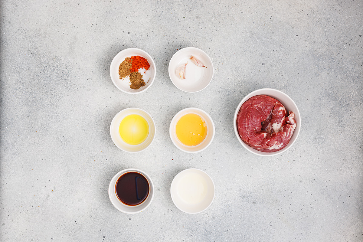 Flat lay of pork tenderloin and marinade ingredients including olive oil, soy sauce, lemon juice, garlic, and spices.