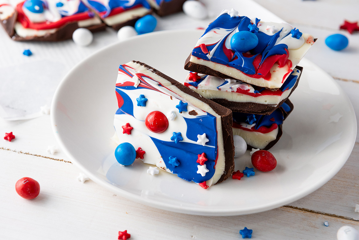 Fourth of July chocolate bark broke into pieces and stacked on a white plate.