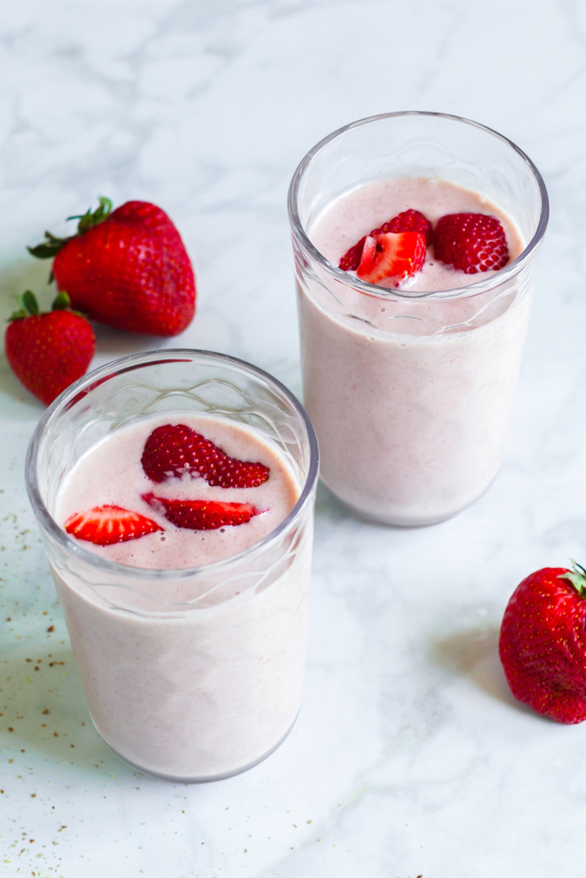 Two glasses of strawberry banana flaxseed smoothie garnished with fresh strawberry slices, surrounded by whole strawberries.