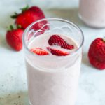 A strawberry banana flaxseed smoothie in a clear glass with fresh strawberries sliced on top.
