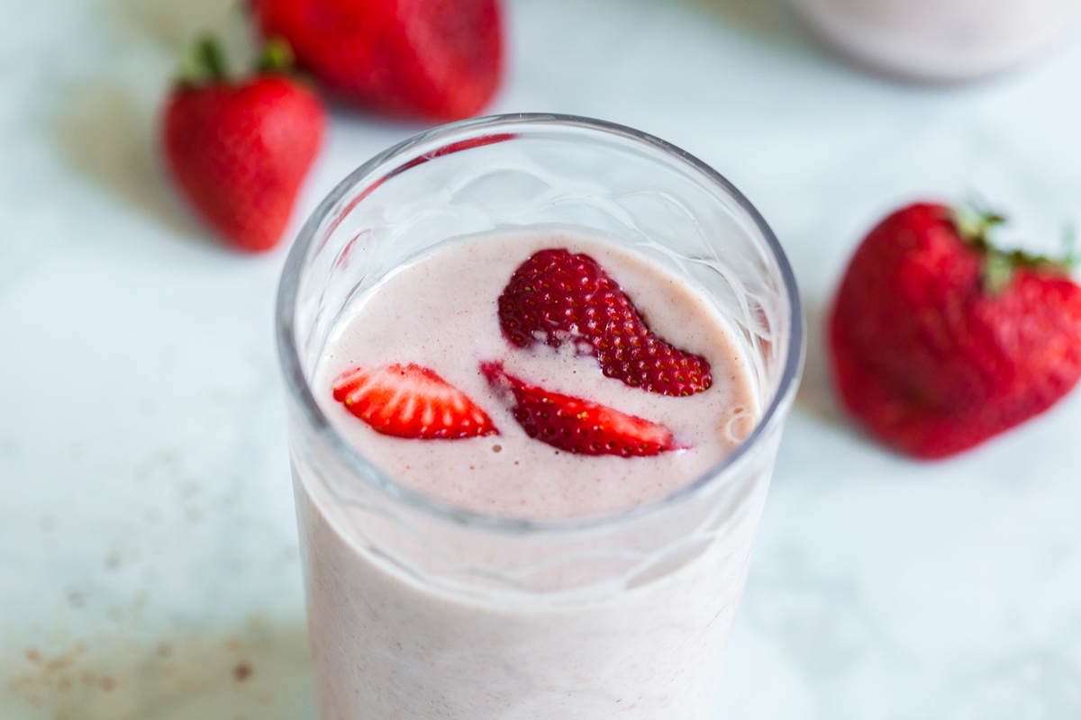 Close-up of strawberry banana flaxseed smoothie in a glass with strawberry slices on top, next to fresh berries.