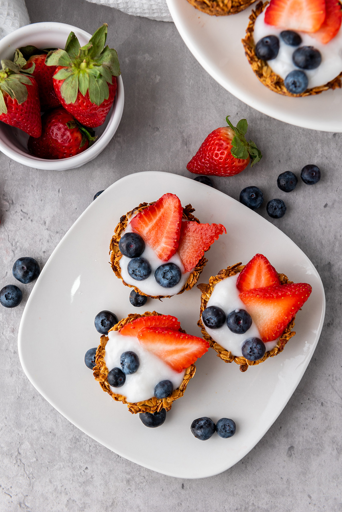 Flat lay of yogurt granola cups on a white plate with fresh fruit, styled for serving.