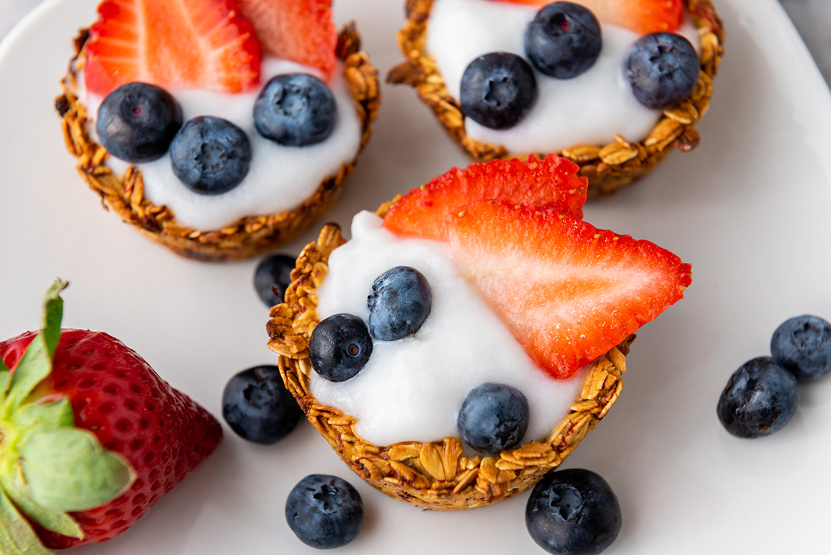 Close-up of yogurt-filled granola cups topped with fresh blueberries and strawberries.