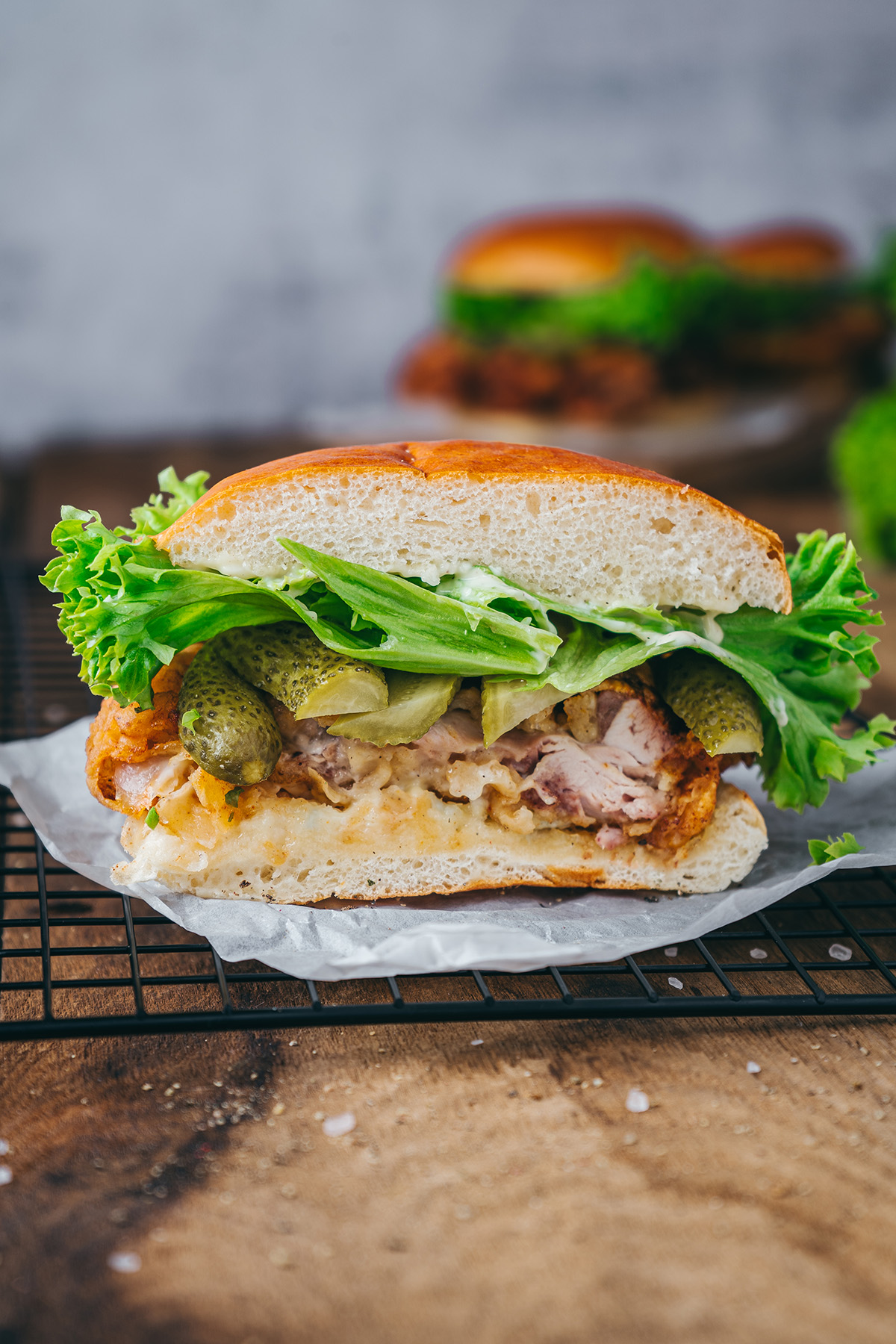 Cross-section of a fried chicken sandwich showing juicy chicken, pickles, lettuce, and sauce on a toasted bun.