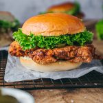 Front view of a homemade buttermilk fried chicken sandwich stacked with lettuce and pickles on a toasted bun.