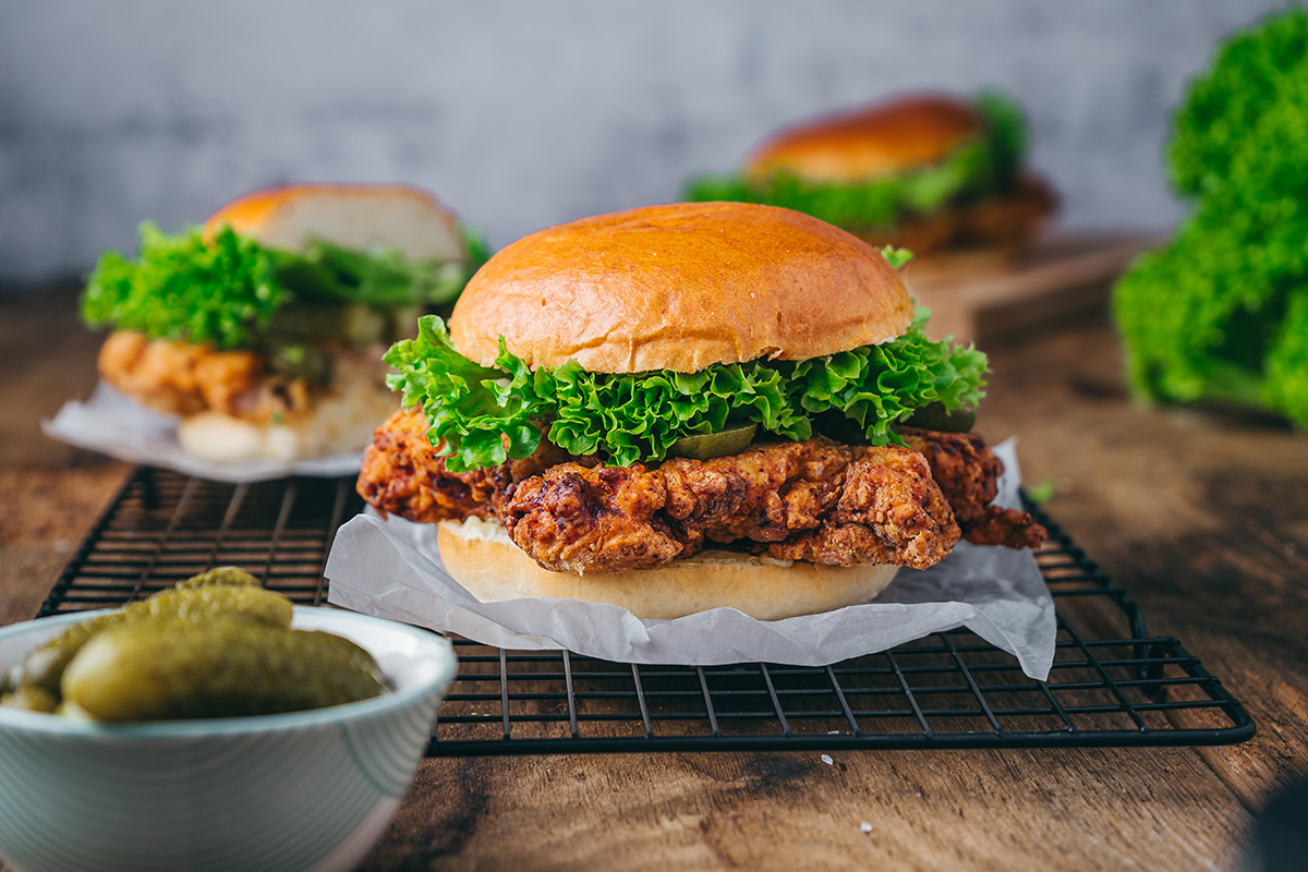 Close-up of a crispy buttermilk fried chicken sandwich with golden bun, fresh lettuce, and pickles.